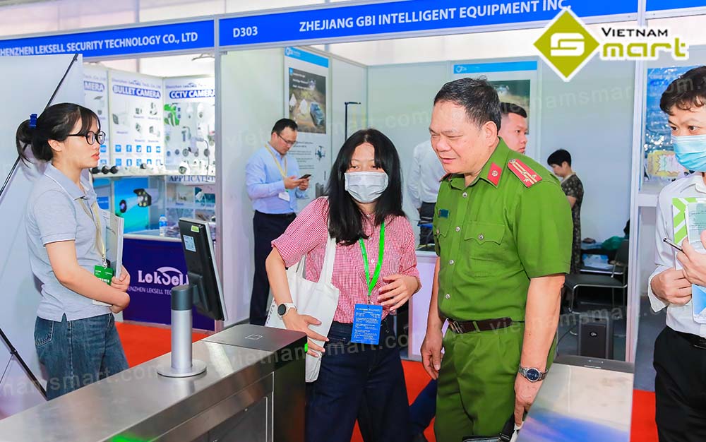 Vietnamsmart trưng bày và giới thiệu thiết bị an ninh tại sự kiện Secutech Vietnam 2023 Nhân viên chăm sóc đang tư vấn khách hàng về xác thực bằng máy chấm công khuôn mặt của cổng xoay ba càng